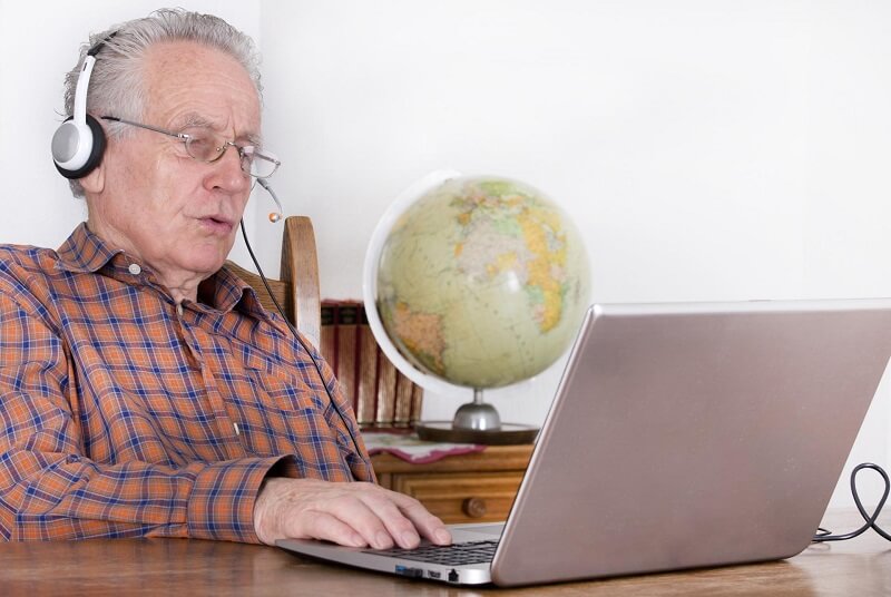 Laptopot és mikrofonos fejhallgatót használó idős férfi